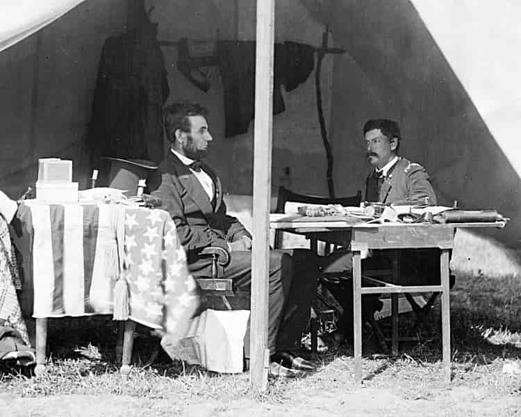 Black and white photograph of Lincoln and McClellan meeting at a table in the general’s tent on the battlefield.